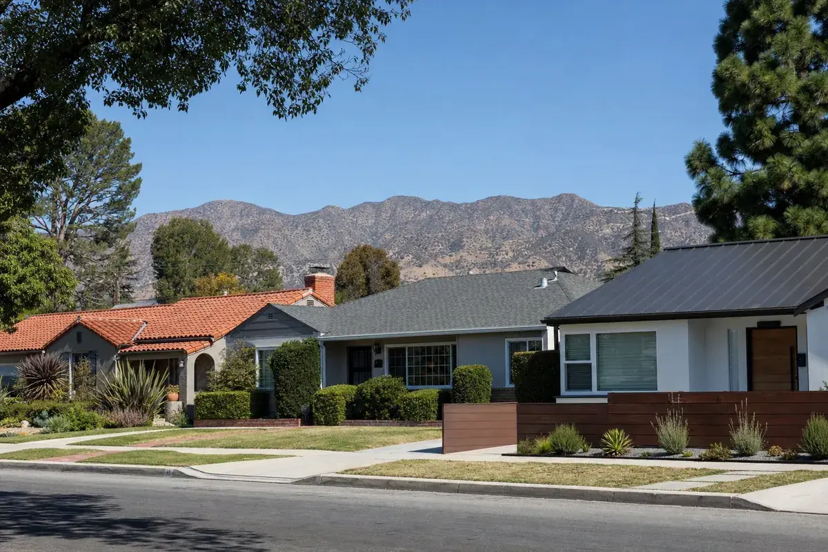 Three neighboring Valley homes with a clay tile roof, a gray asphalt shingle roof, and a dark standing-seam metal roof, with mountains behind